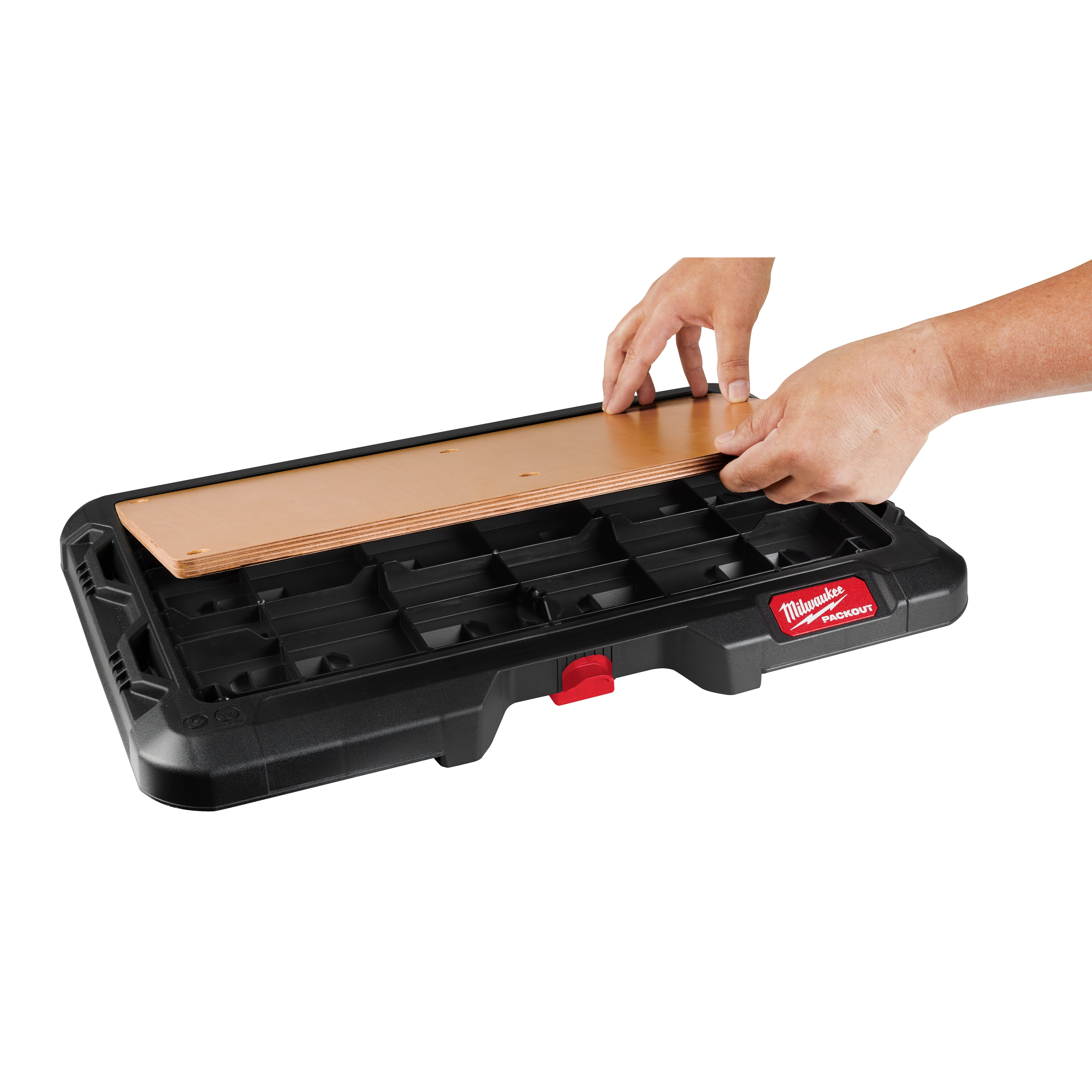 Hands placing a wooden panel on the PACKOUT Customizable Work Top, a black and red workbench with compartments.