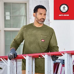 Man wearing an olive green GRIDIRON Pocket T-Shirt - Long Sleeve, standing next to a red ladder with gloves, "Anti-Odor" badge visible.