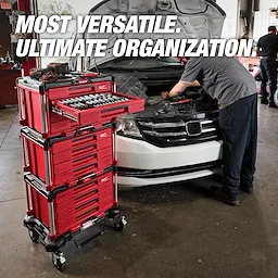 The Milwaukee Packout modular storage system is shown in a garage next to a mechanic working on a car. The red and black stacked toolboxes are labeled with the brand's logo. A drawer with tools is pulled out, and promotional text reads: "Most versatile. Ultimate organization."