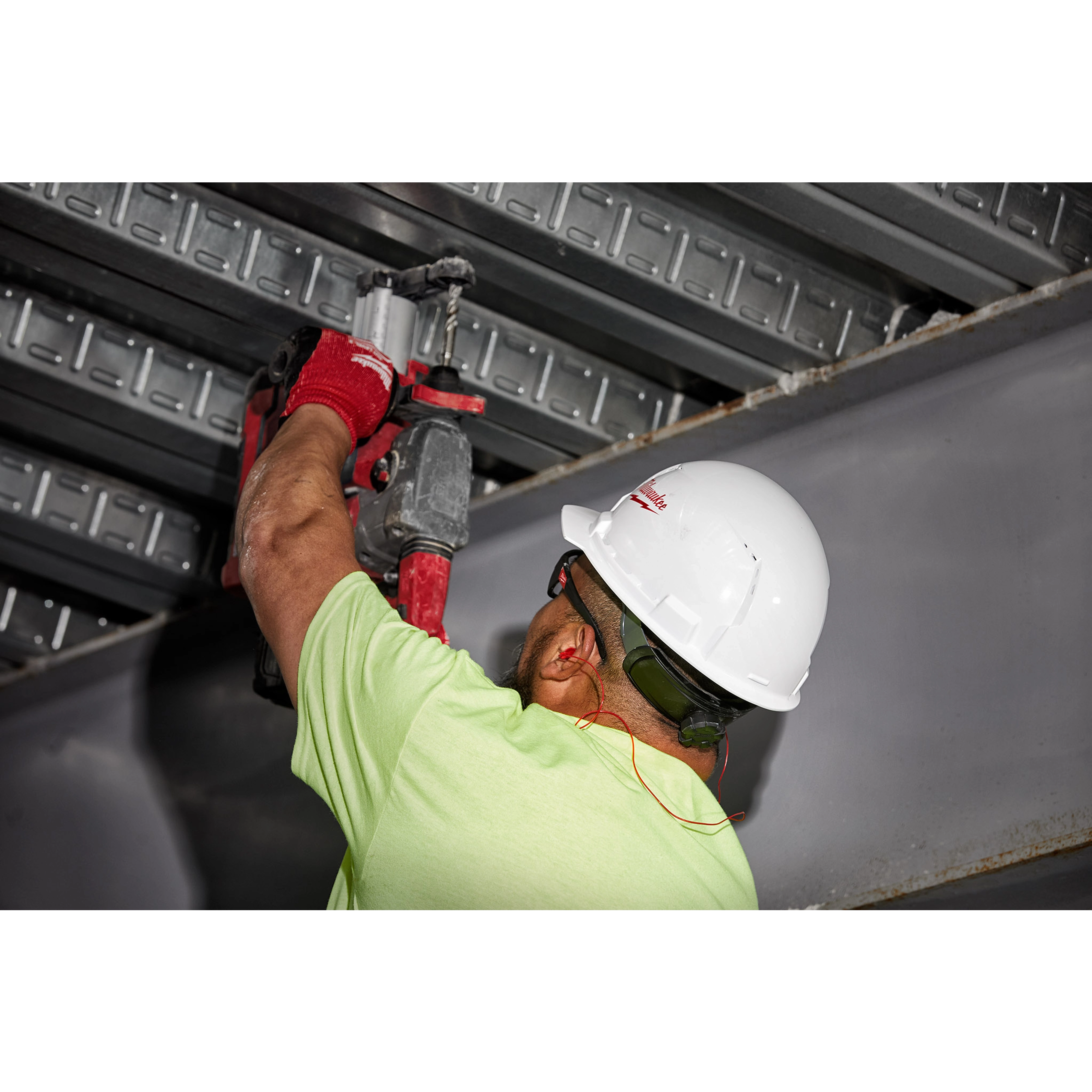 Worker in a light green shirt and white hard hat drilling overhead, wearing red gloves and Corded Ear Plugs for hearing protection.