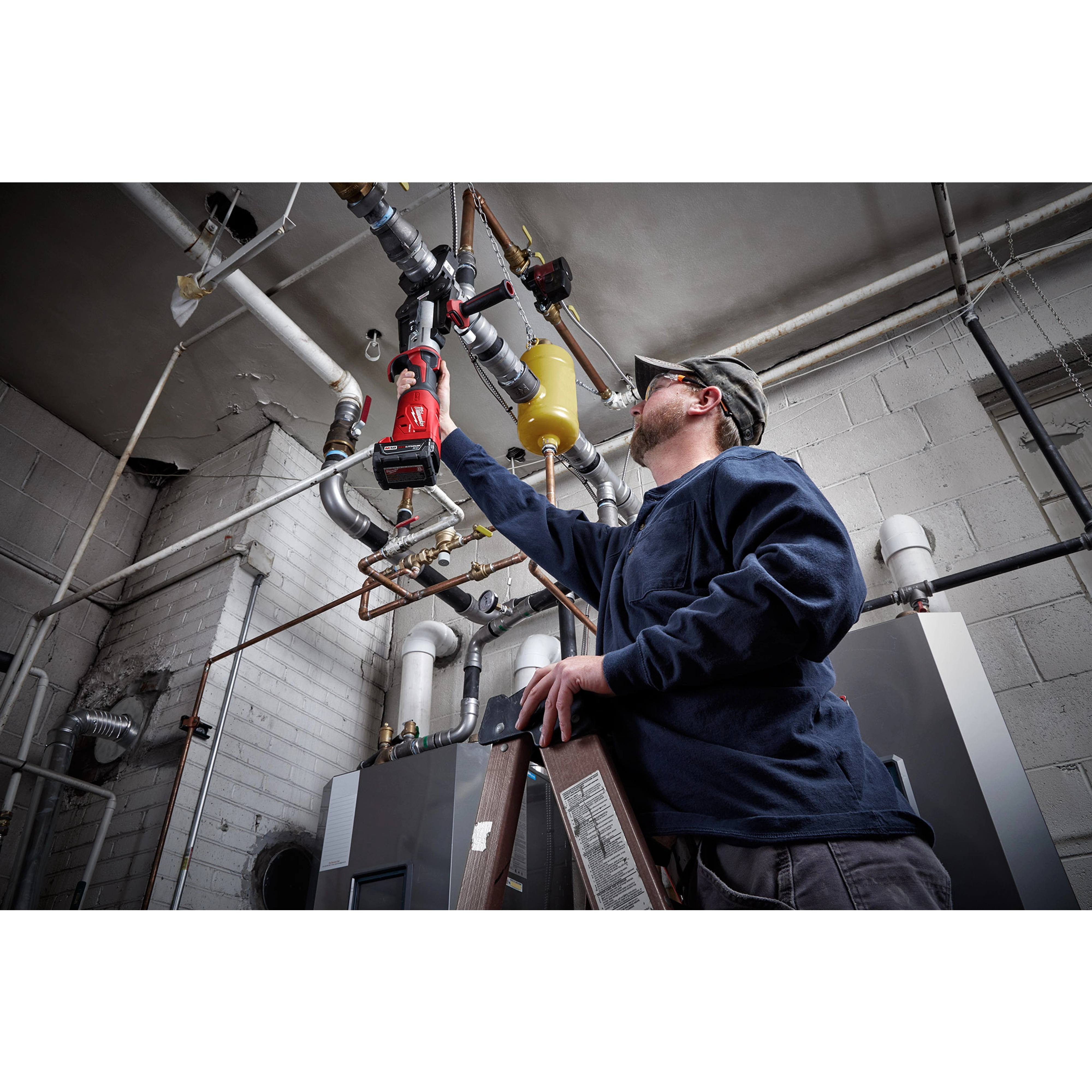 A man uses a 2½” - 4” IPS XL Ring Kit for M18 FORCE LOGIC Long Throw Press Tool to work on industrial piping in a mechanical room.