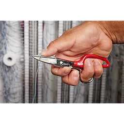 A hand is holding Electrician Scissors with Extended Handle while cutting a blue wire. Coiled cables are visible in the background.