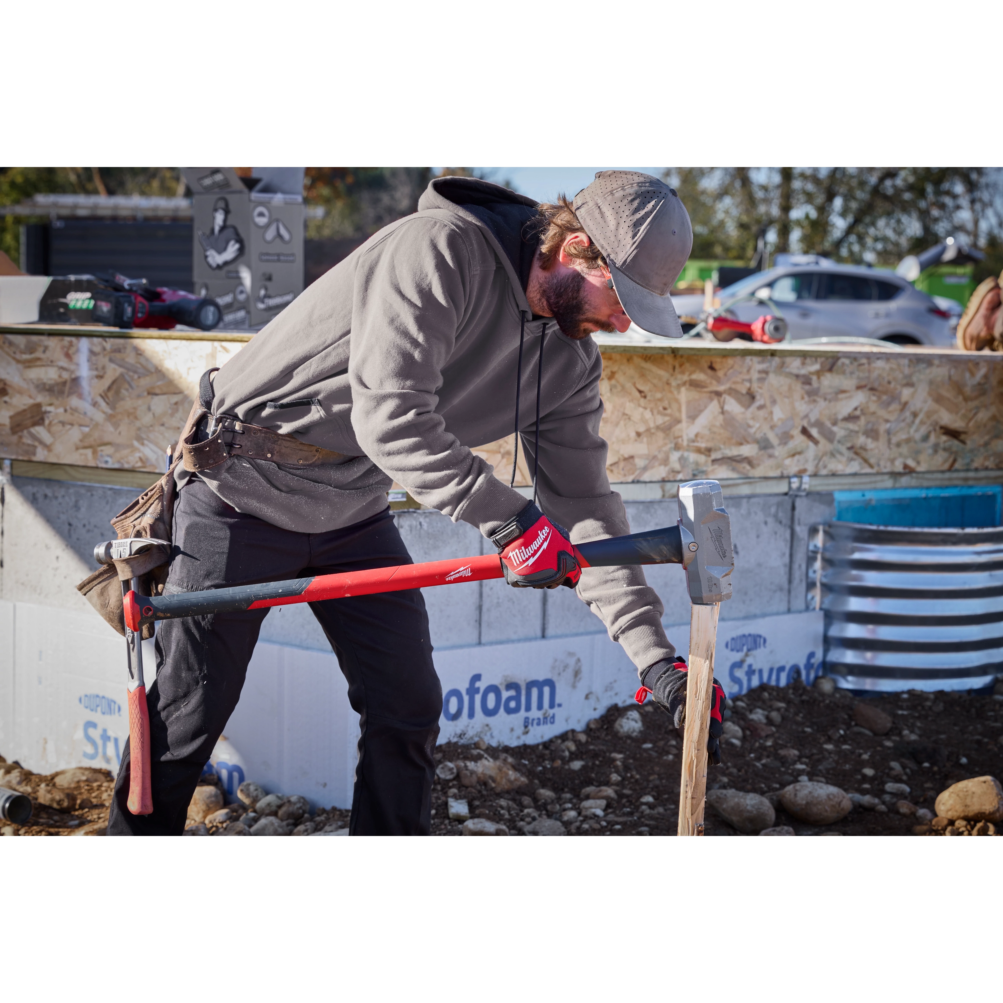 A person using a 10lb Sledge Hammer (34" Handle) to drive a post into the ground at a construction site.