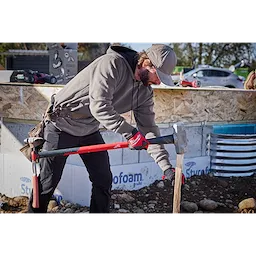 A person using a 10lb Sledge Hammer (34" Handle) to drive a post into the ground at a construction site.