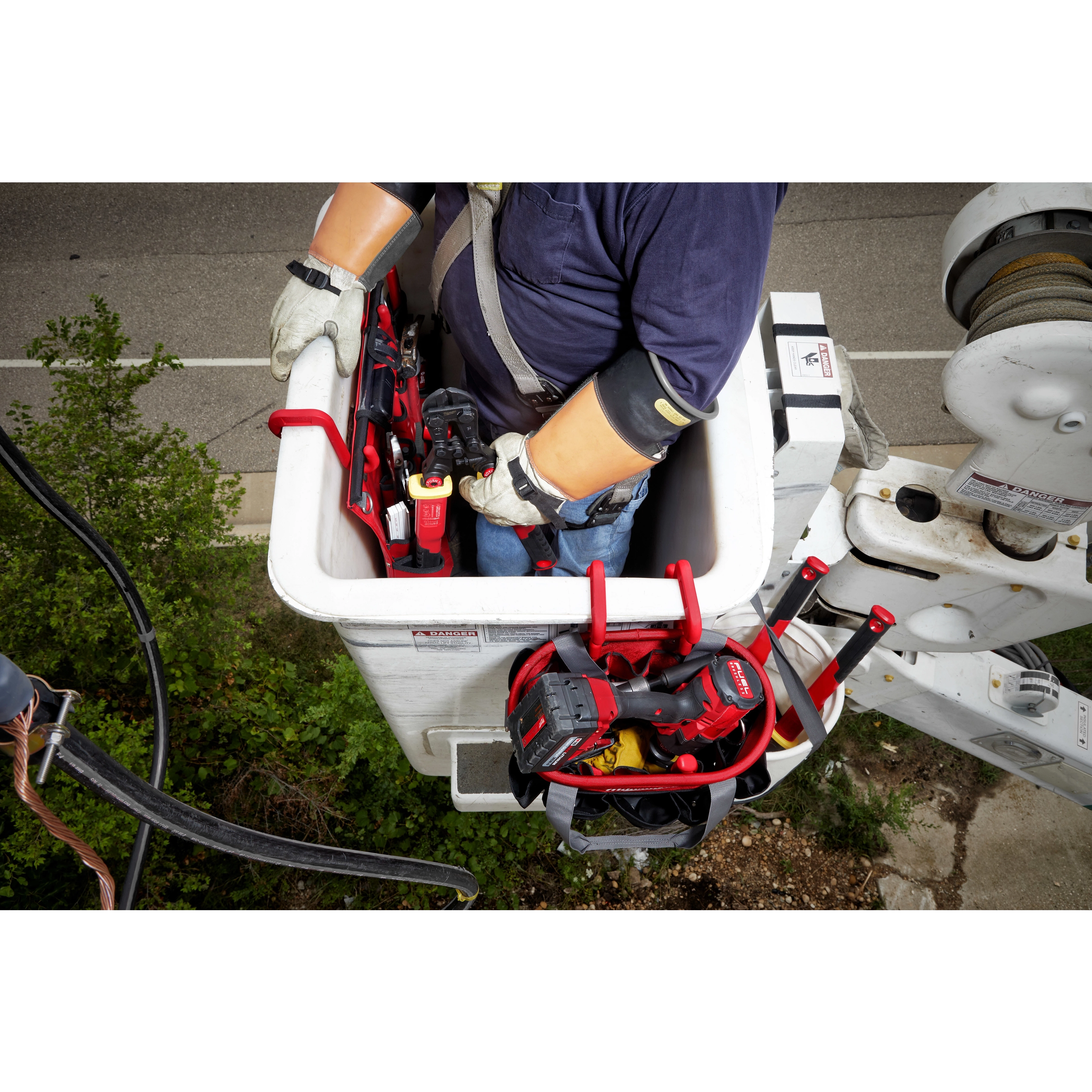 A worker in a utility bucket uses the 2 Inch Bucket Hook to hang various tools and equipment over the edge for easy access.
