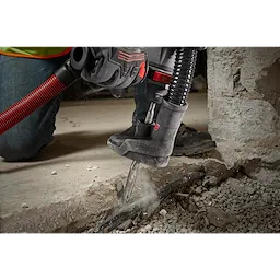 A person using the SDS+ SLEDGE 3/4"X10" FLAT CHISEL attached to a power tool to break up a concrete surface.