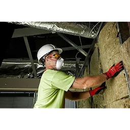 Worker installing insulation while wearing a white helmet, gloves, and Safety Glasses - Yellow Fog-Free Lenses in a construction setting.