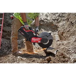 A construction worker uses a Milwaukee MX FUEL 14-inch Cut-Off Saw with RAPIDSTOP App Shot to cut a pipe in a dirt trench.