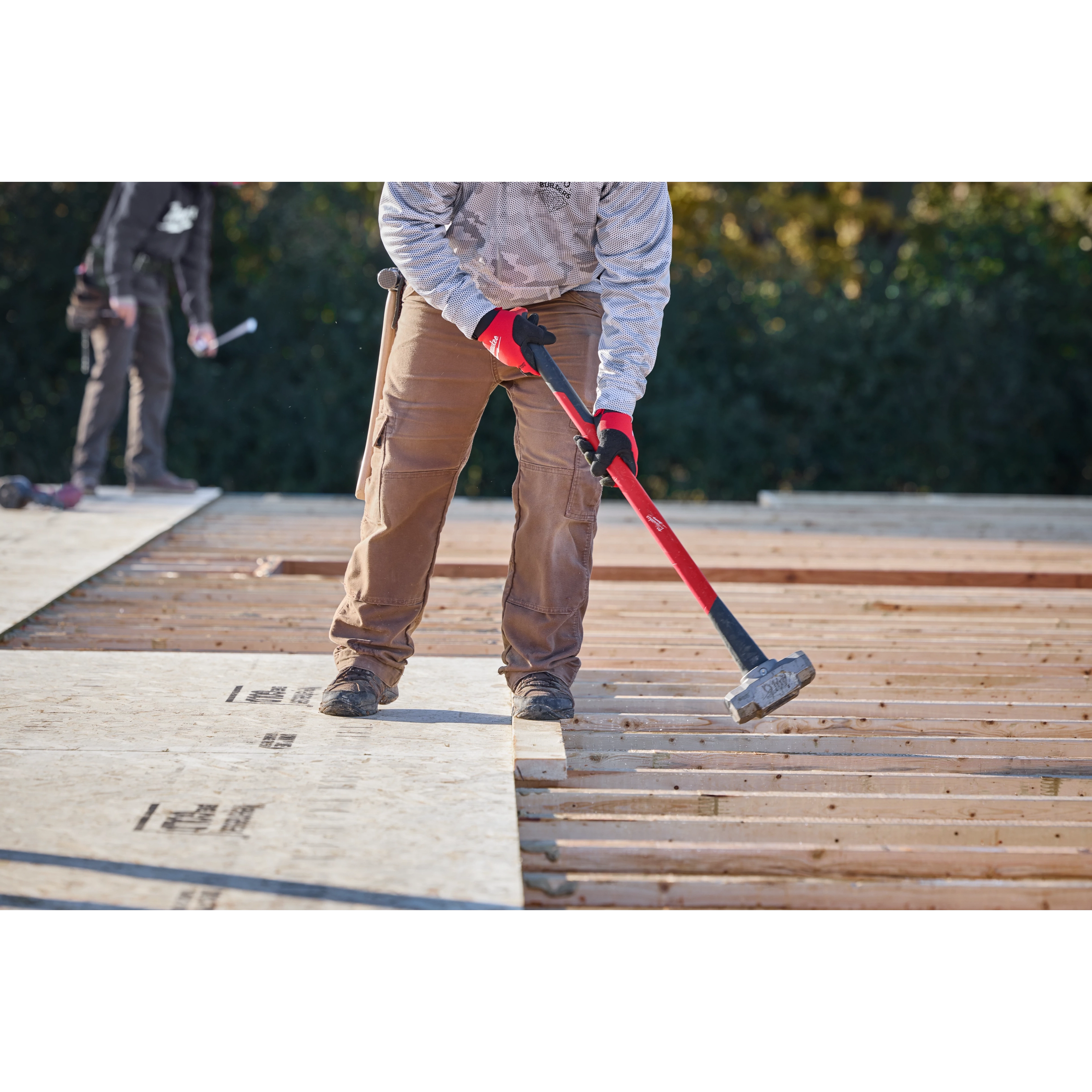 A worker using an 8lb sledgehammer (34" handle) to secure plywood sheets on a construction site.