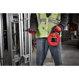 Person holding a 1/8" 50' Steel Fish Tape, wearing a hi-visibility vest and gloves, in a construction site with metal framing.