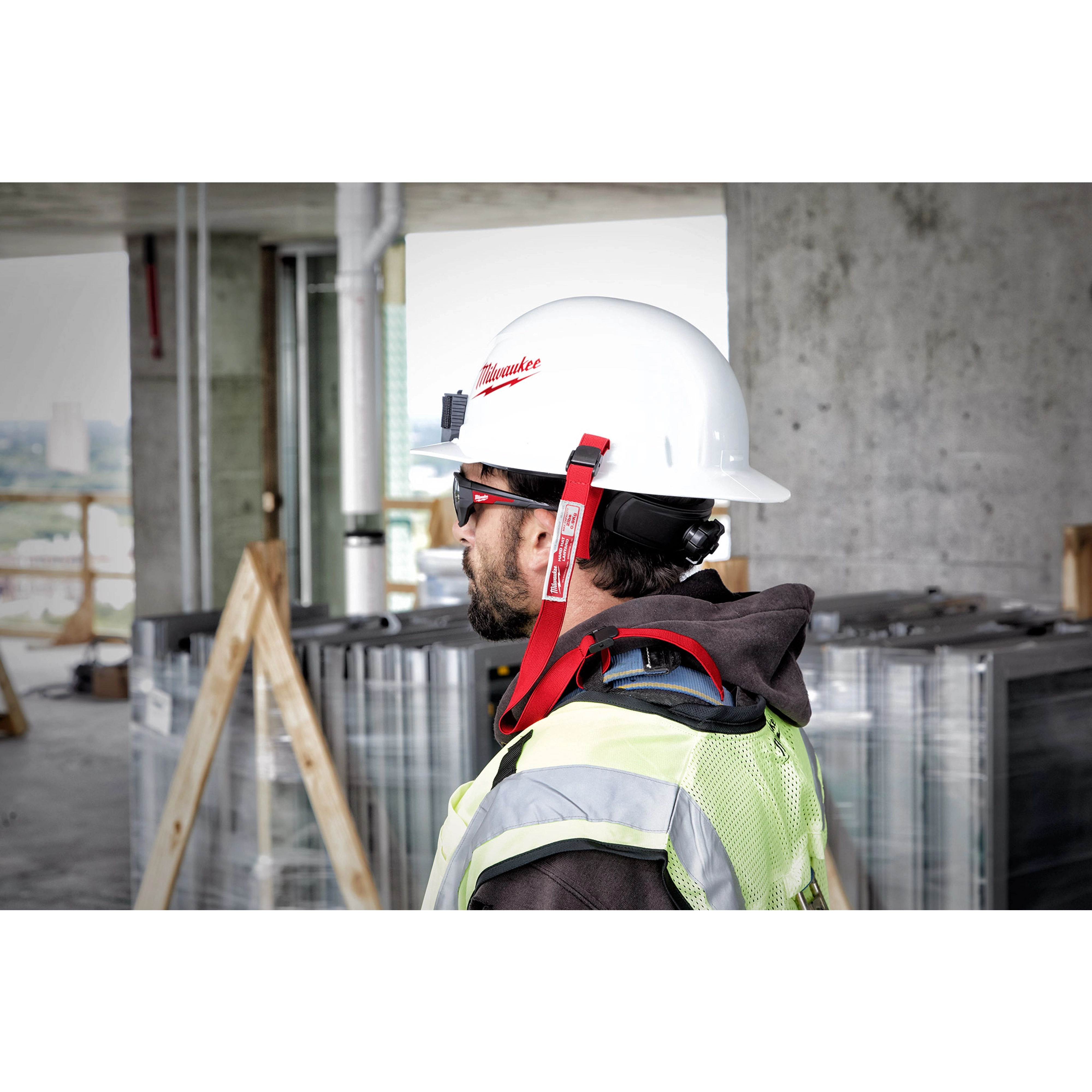 Worker wearing a white hard hat secured with a red Hard Hat Lanyard with Loop, standing at a construction site.