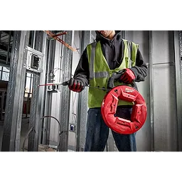 Worker using a 100% Polyester Fish Tape with Flexible Leader in a metal-framed construction site, wearing a green safety vest and red gloves.