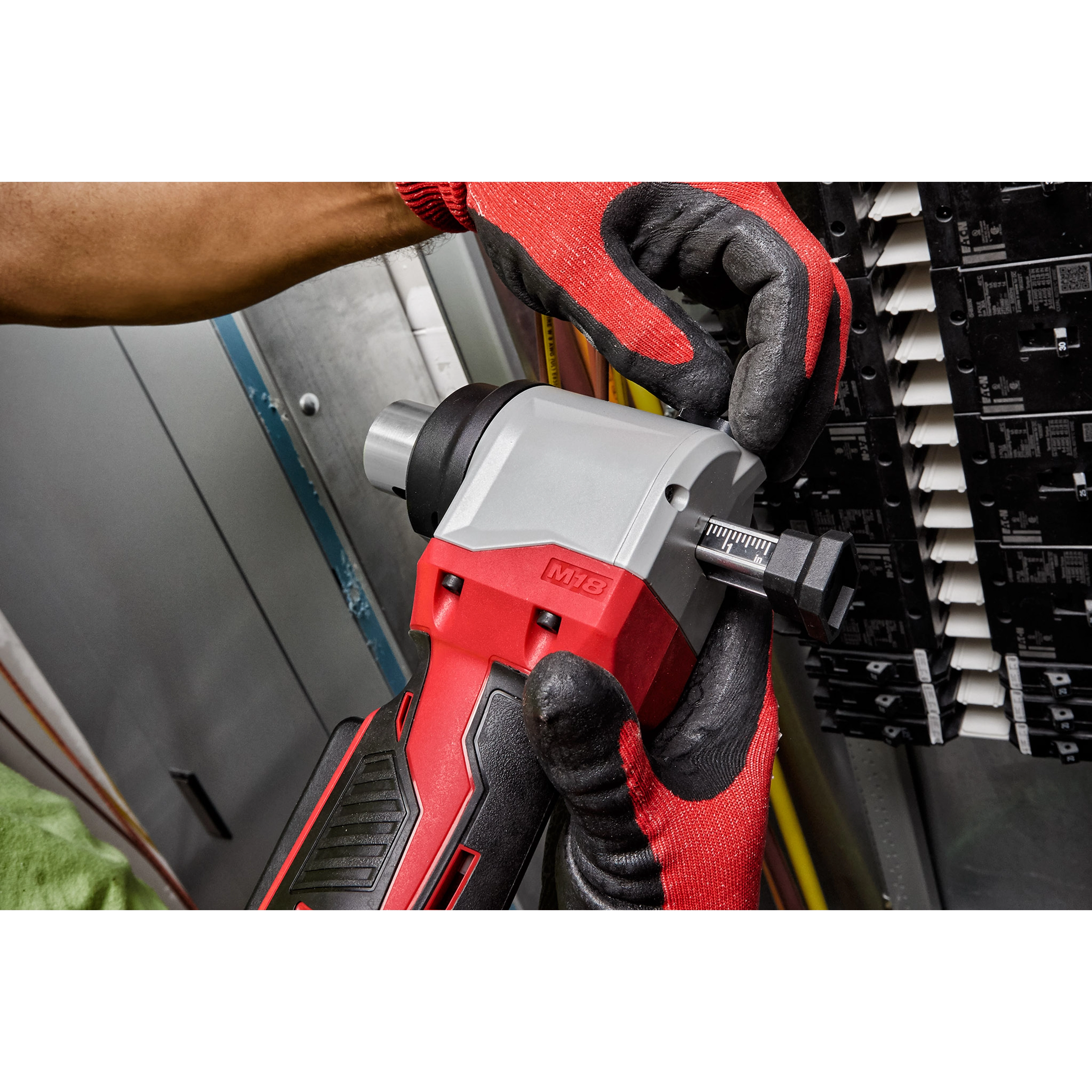A person wearing red gloves uses the M18 Cable Stripper to work on electrical wiring in an industrial setting.