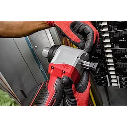 A person wearing red gloves uses the M18 Cable Stripper to work on electrical wiring in an industrial setting.