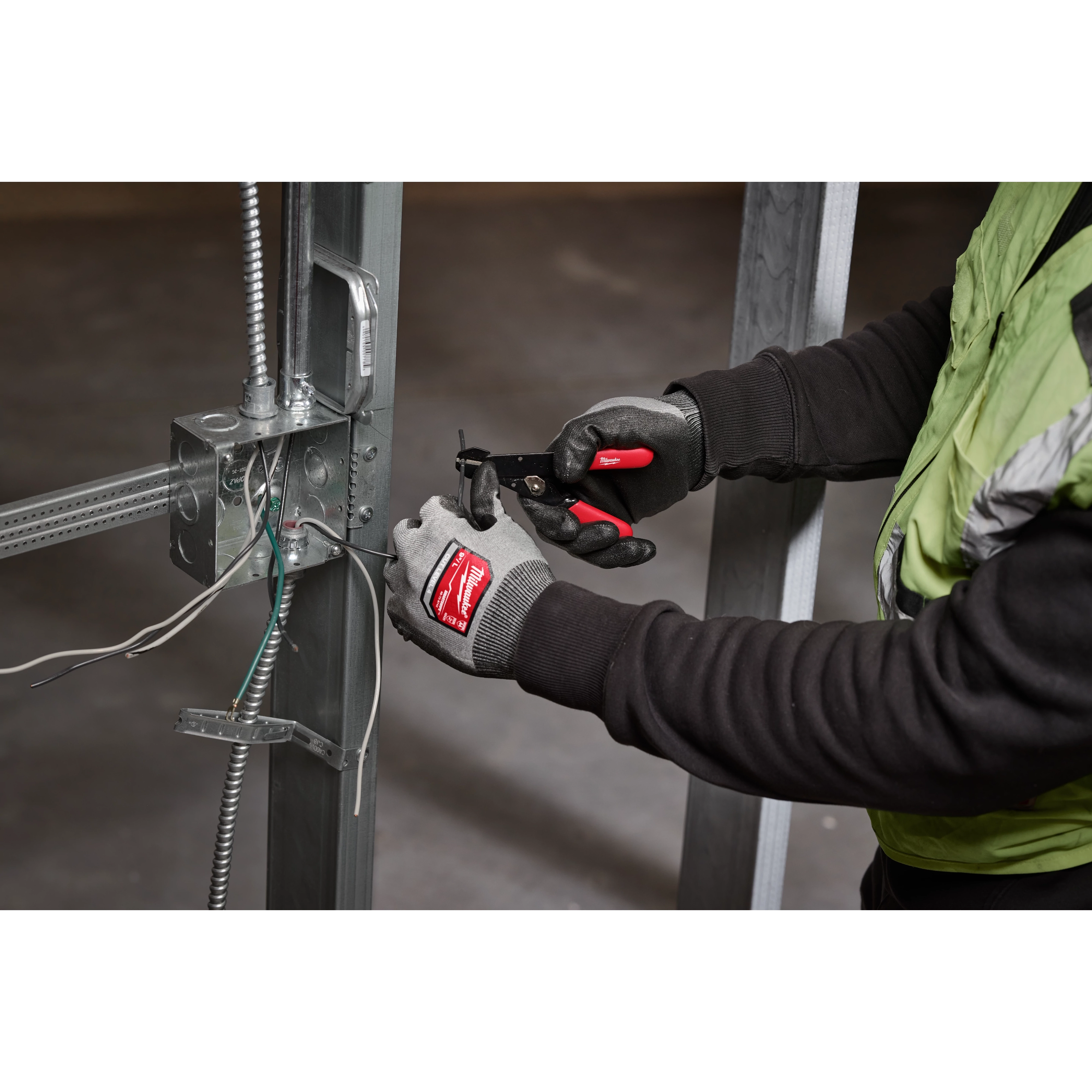 A person wearing gloves uses a 10-24 AWG Adjustable Compact Wire Stripper & Cutter to strip wires connected to a metal frame.
