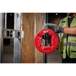 A construction worker uses a 120' 1/8" Stainless Steel Fish Tape with a red and black handle to thread wiring through metal studs.