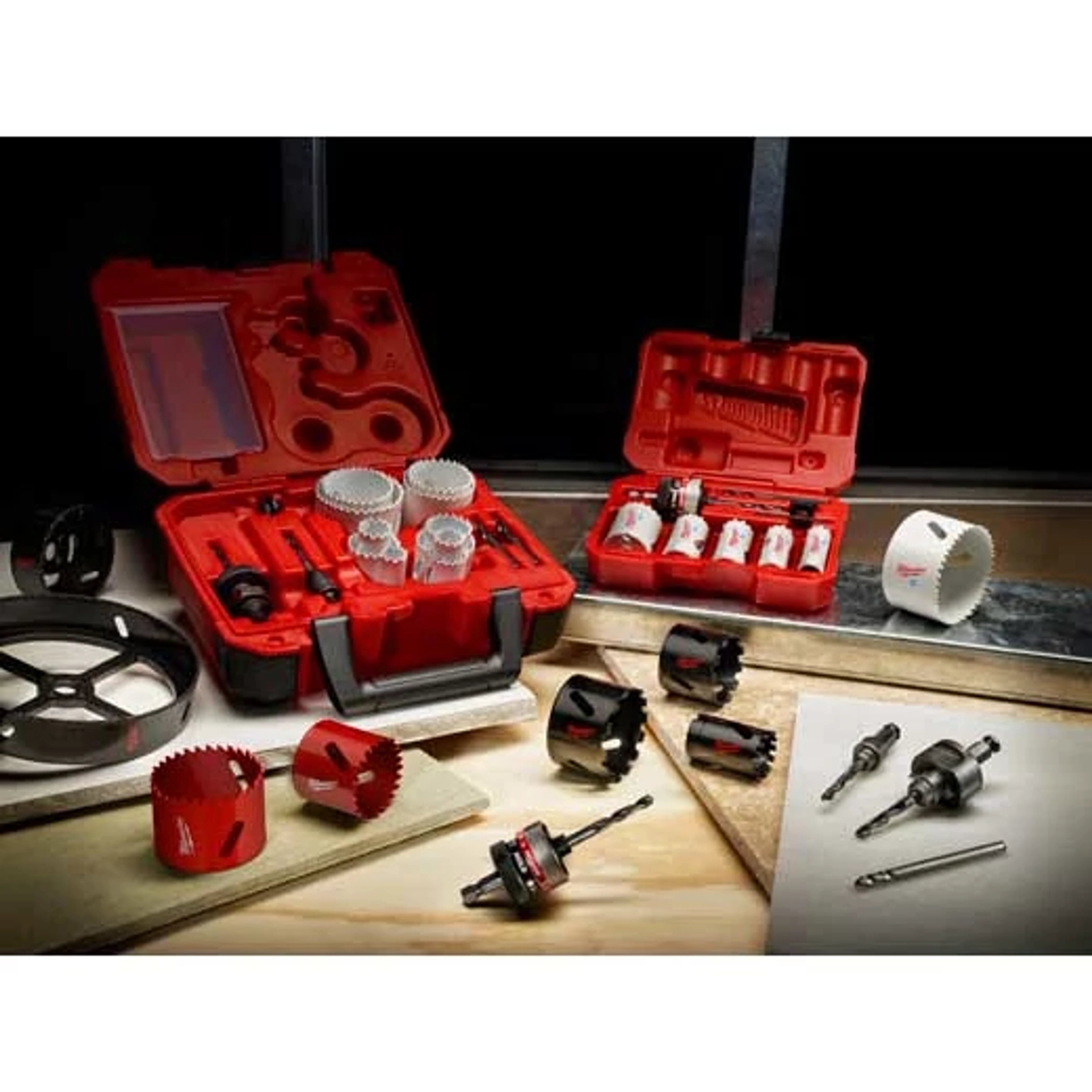 Carbide%20Grit%20Hole%20Saw product consisting of red and white hole saws displayed in red carrying cases. Various sizes of saws and two drill bits are spread on a wooden surface alongside the cases, suggesting a comprehensive set suitable for drilling. Includes both open and closed case arrangements.