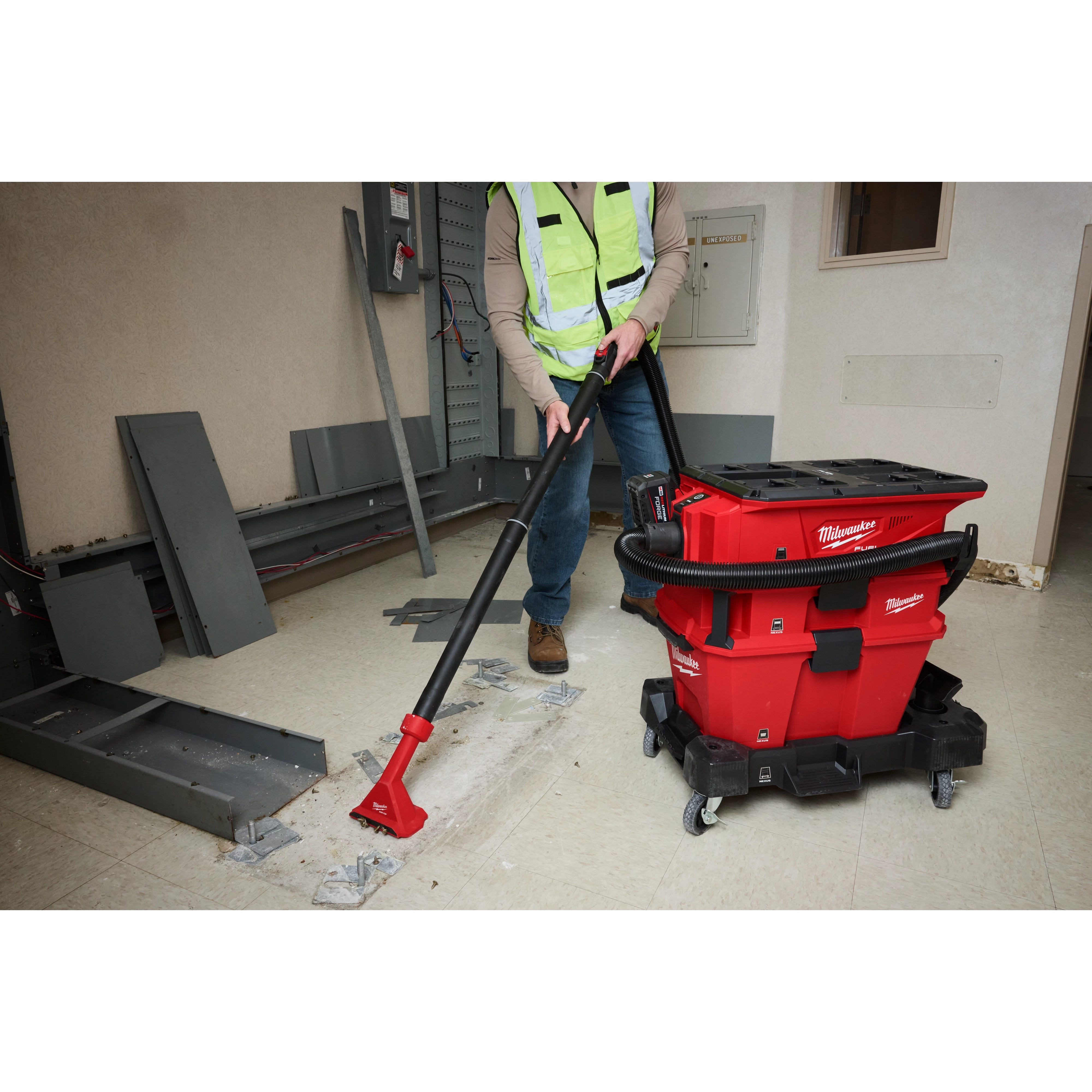 A worker uses the NEXUS™ Dedicated Debris Separator to clean debris on a construction site. The red and black machine has hoses attached and is mounted on wheels for easy mobility. The worker wears a reflective vest and operates the vacuum with a wide nozzle attachment.