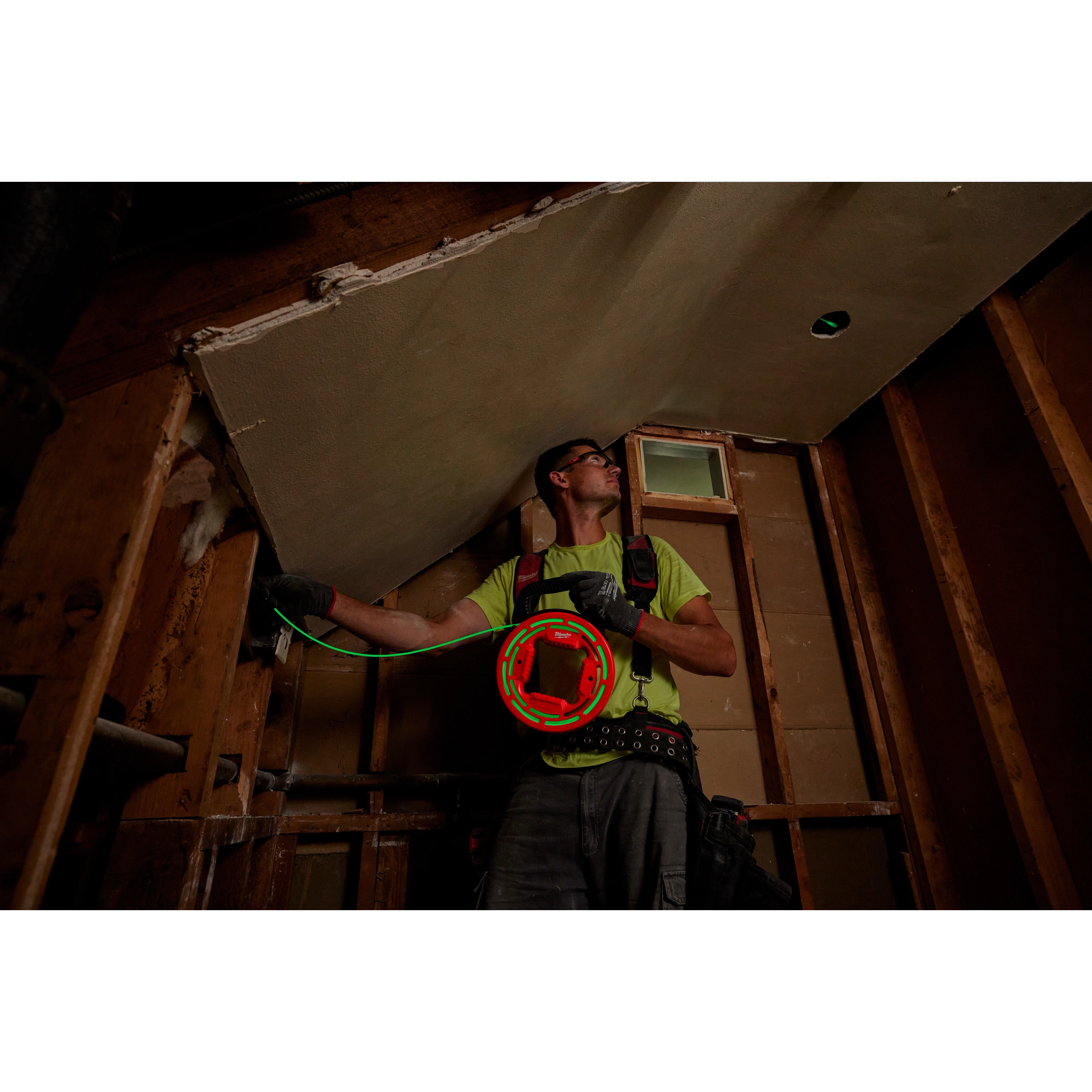 A construction worker uses the 40%27%20Glow%20Fish%20Tape to feed wiring through a ceiling in a partially completed room.