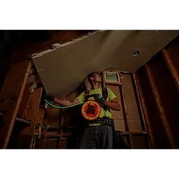 A construction worker uses the 40%27%20Glow%20Fish%20Tape to feed wiring through a ceiling in a partially completed room.