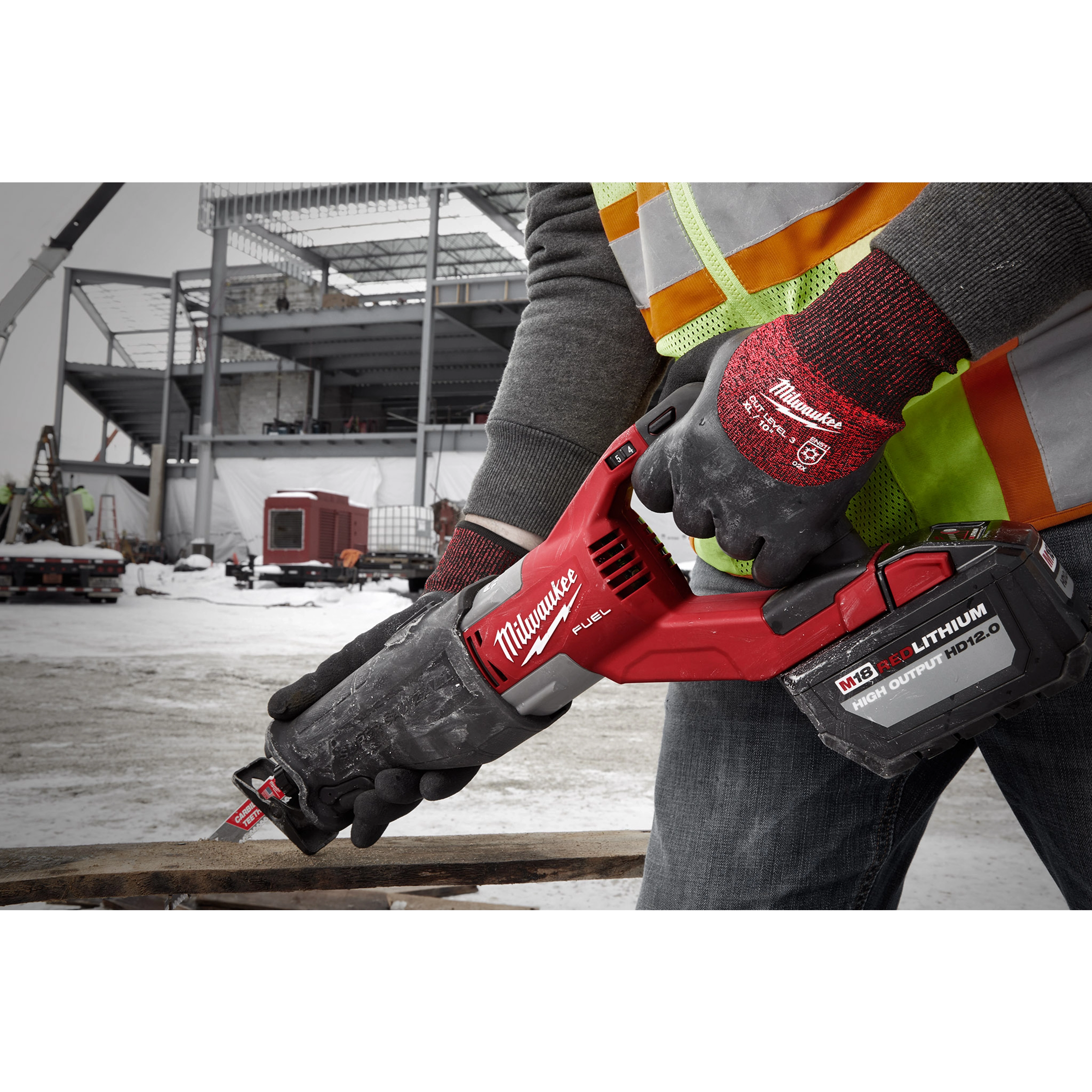 Person wearing Cut Level 3 Winter Insulated Gloves - XL holding a red power tool on a snowy construction site.