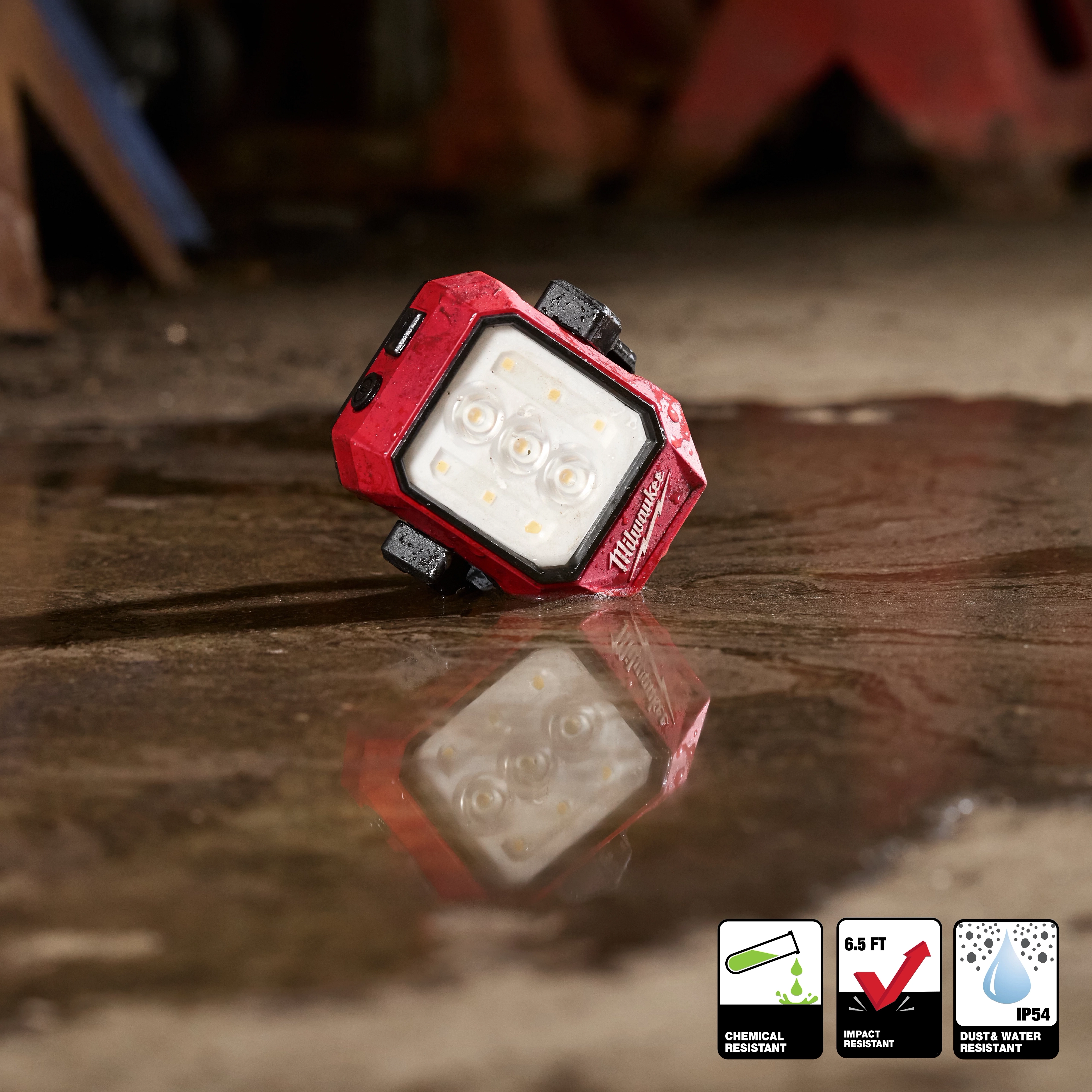 Milwaukee Rechargeable Pivoting Task Light w/ Spot Mode lying on a wet concrete floor with its reflection visible.