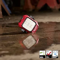 Milwaukee Rechargeable Pivoting Task Light w/ Spot Mode lying on a wet concrete floor with its reflection visible.