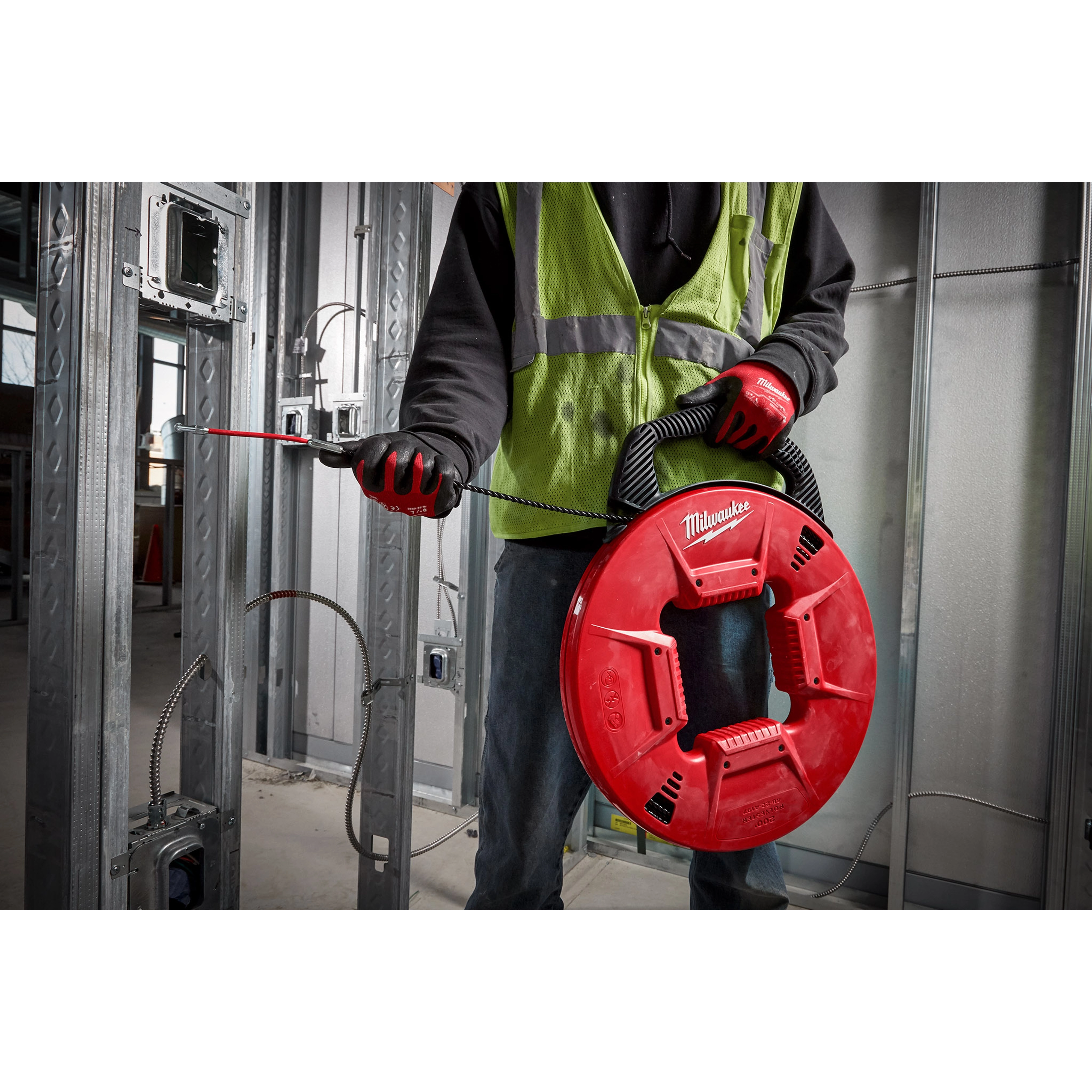 Person using the 200% Polyester Fish Tape w/ Flexible Leader to guide electrical wire through metal framing in a construction site.