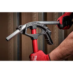 A person wearing red gloves uses a 3/4" EMT Iron Conduit Bender to bend a metal conduit. The bender features angle marks and a red handle.