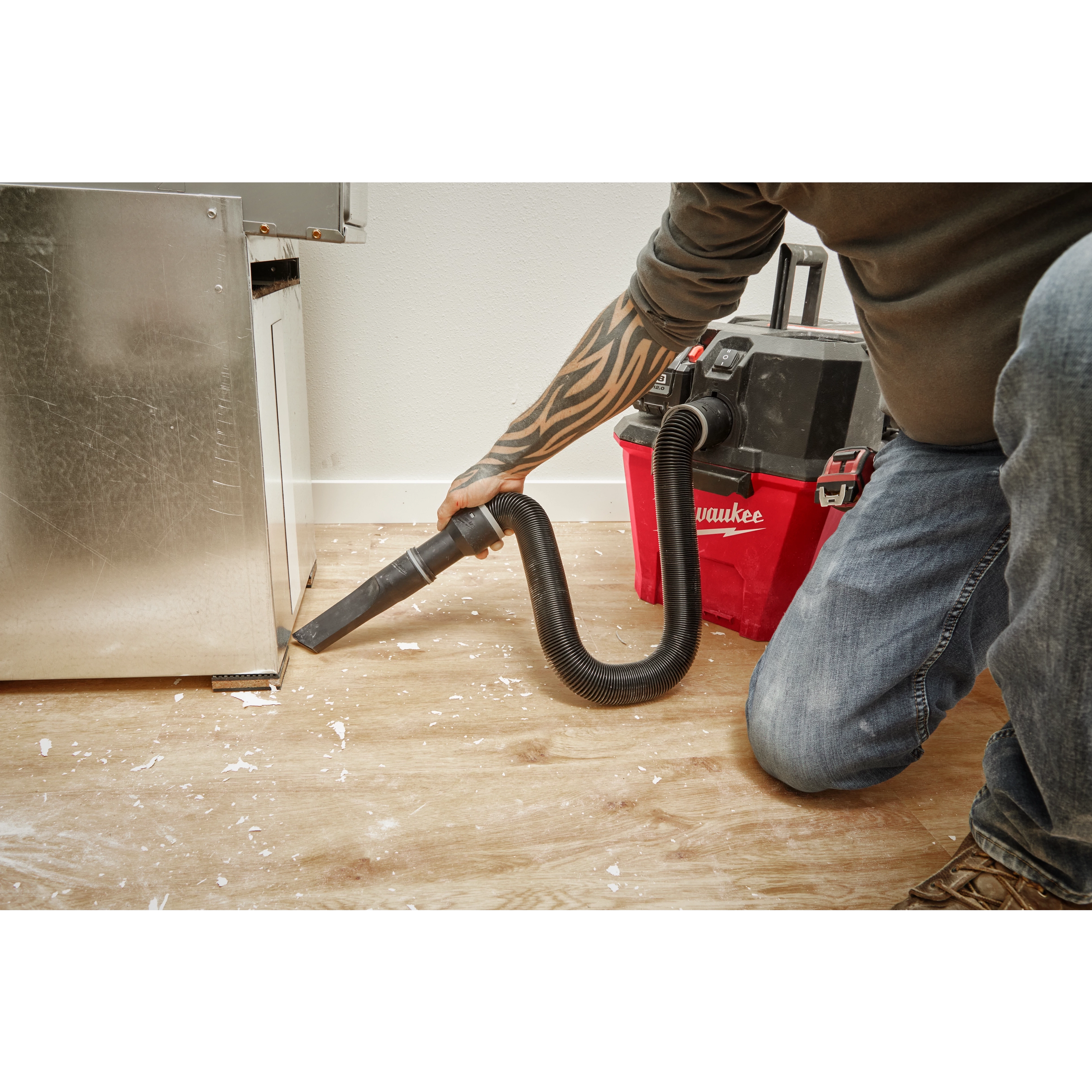 A person uses a vacuum cleaner with a 1-7/8” x 32” to 102” Expandable Hose to clean debris from a hardwood floor next to a cabinet.