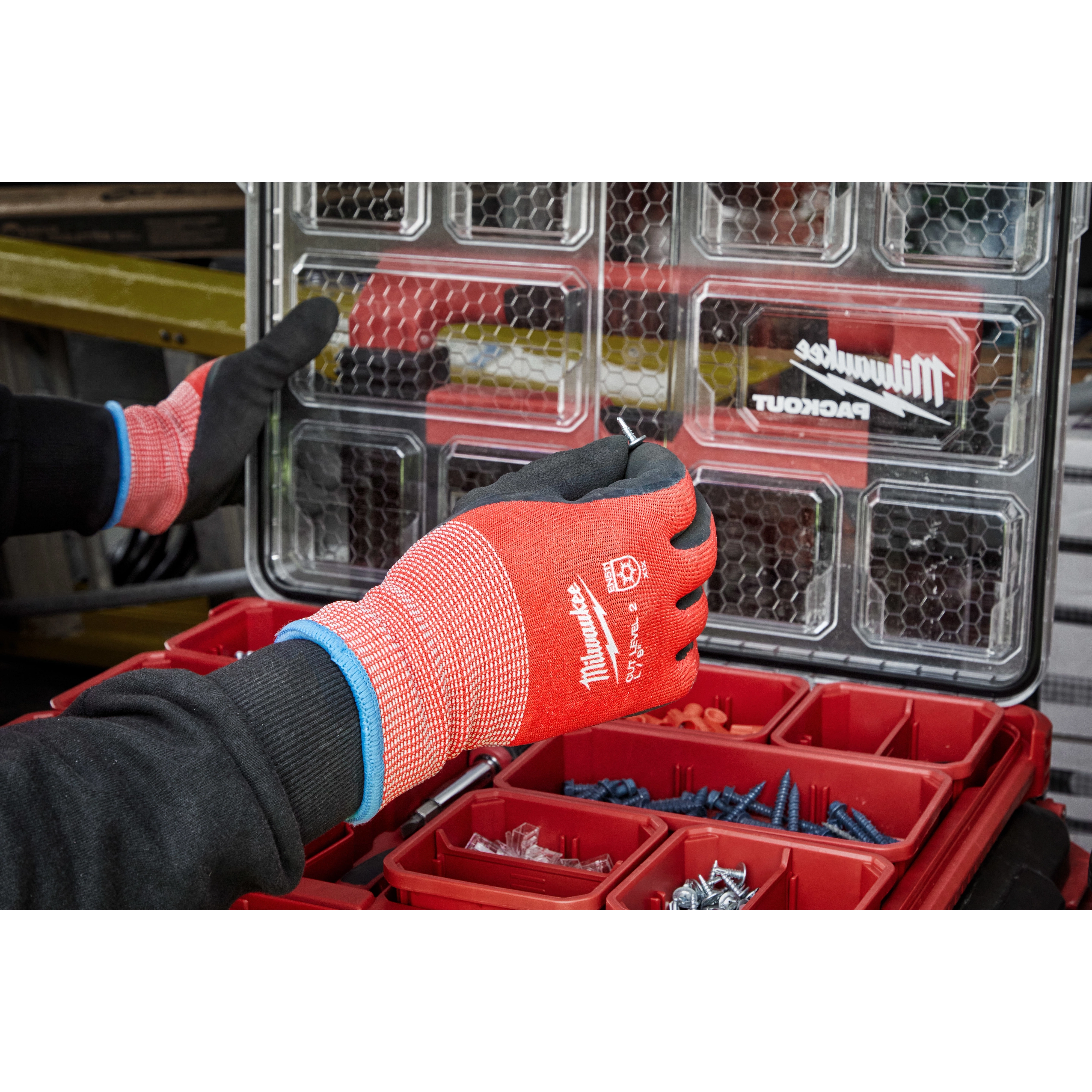 Person wearing Cut Level 2 Winter Dipped Gloves - L while handling screws from a red organizational case with compartments. The gloves are red with black palms, designed for protection and warmth in winter conditions.
