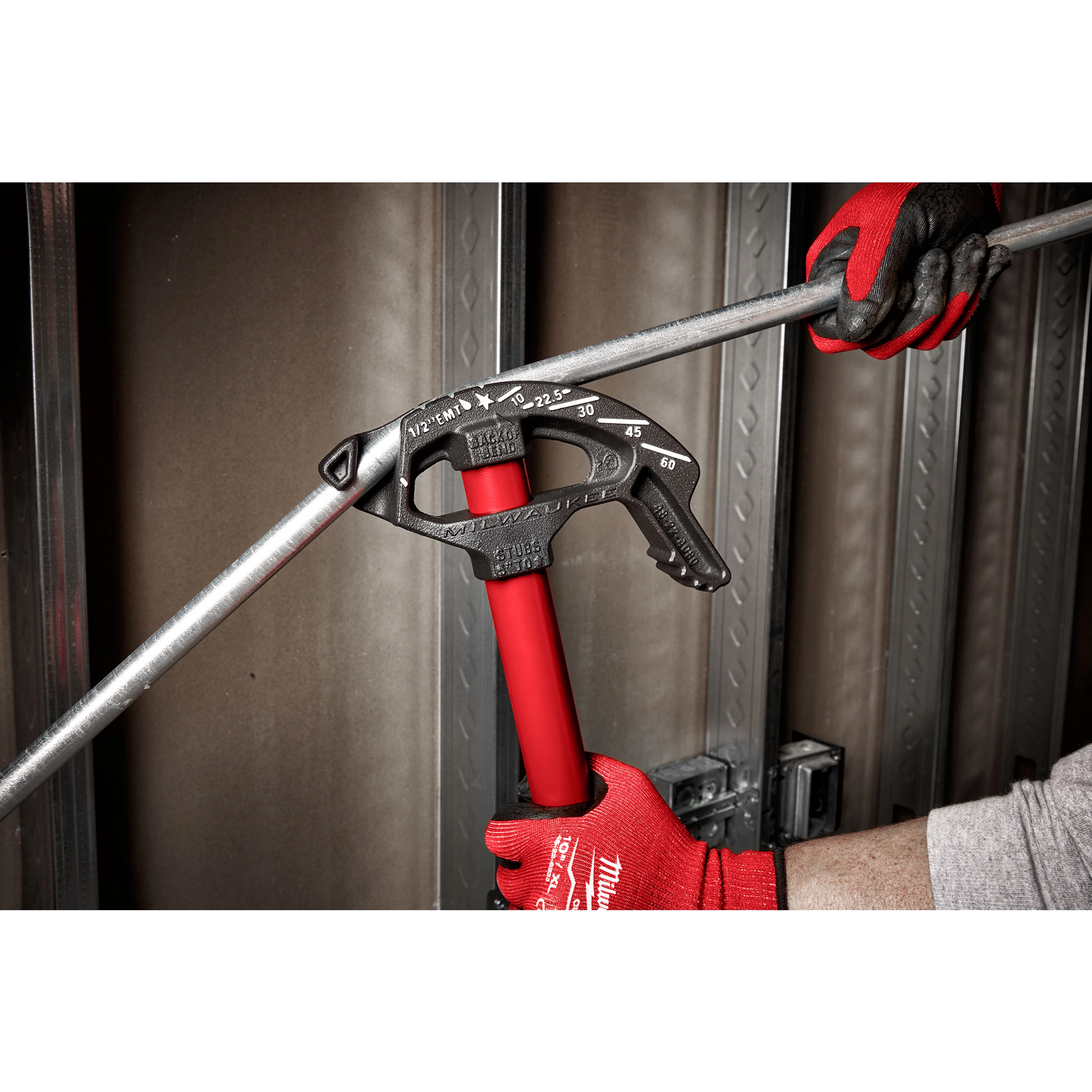 1/2" EMT Iron Conduit Bender with red handle, used by a person wearing red work gloves to bend conduit pipe in a construction setting.