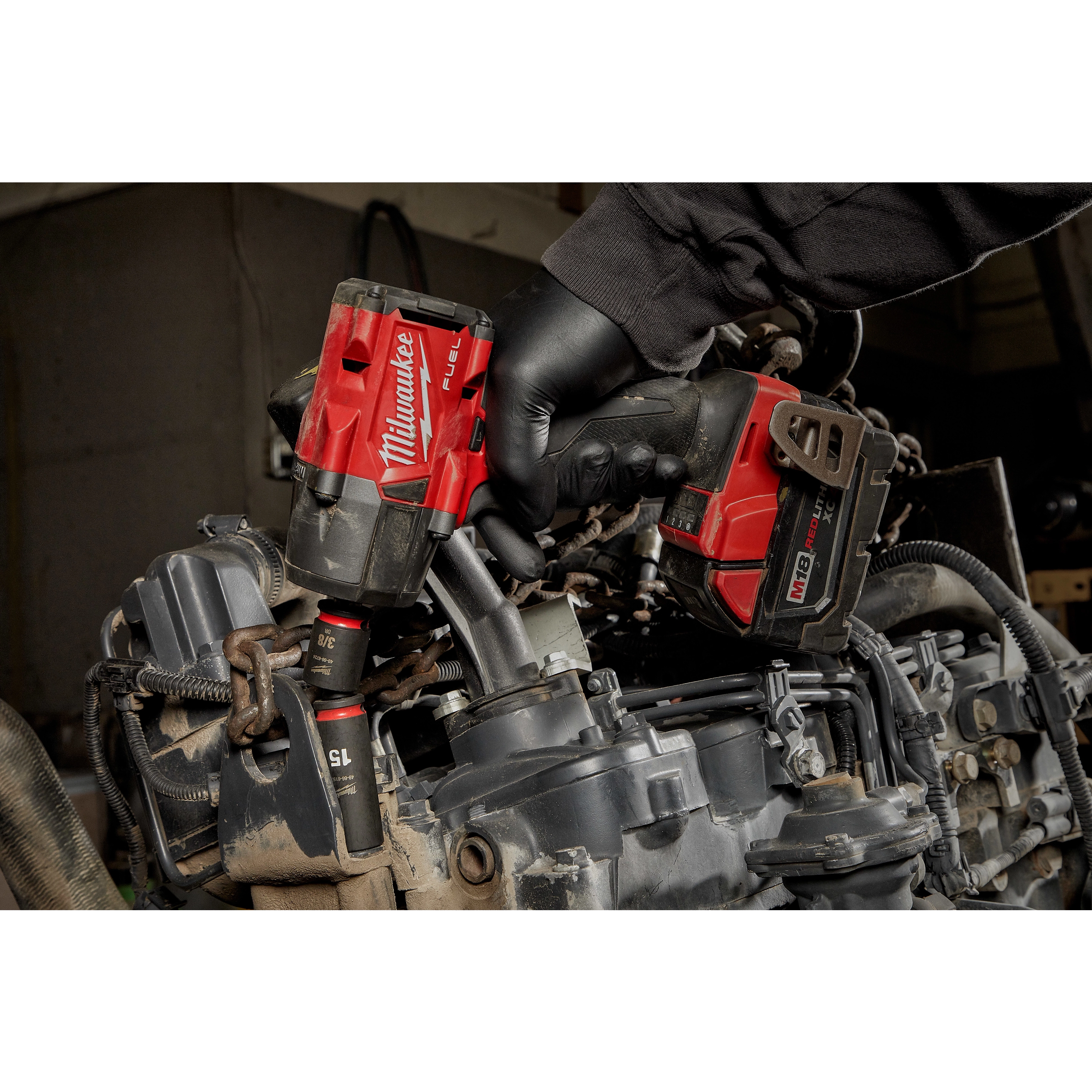 Red Milwaukee Fuel impact wrench using SHOCKWAVE Impact Duty 3/8" Drive 15MM Deep 6 Point Socket on an engine, with a person’s hand.
