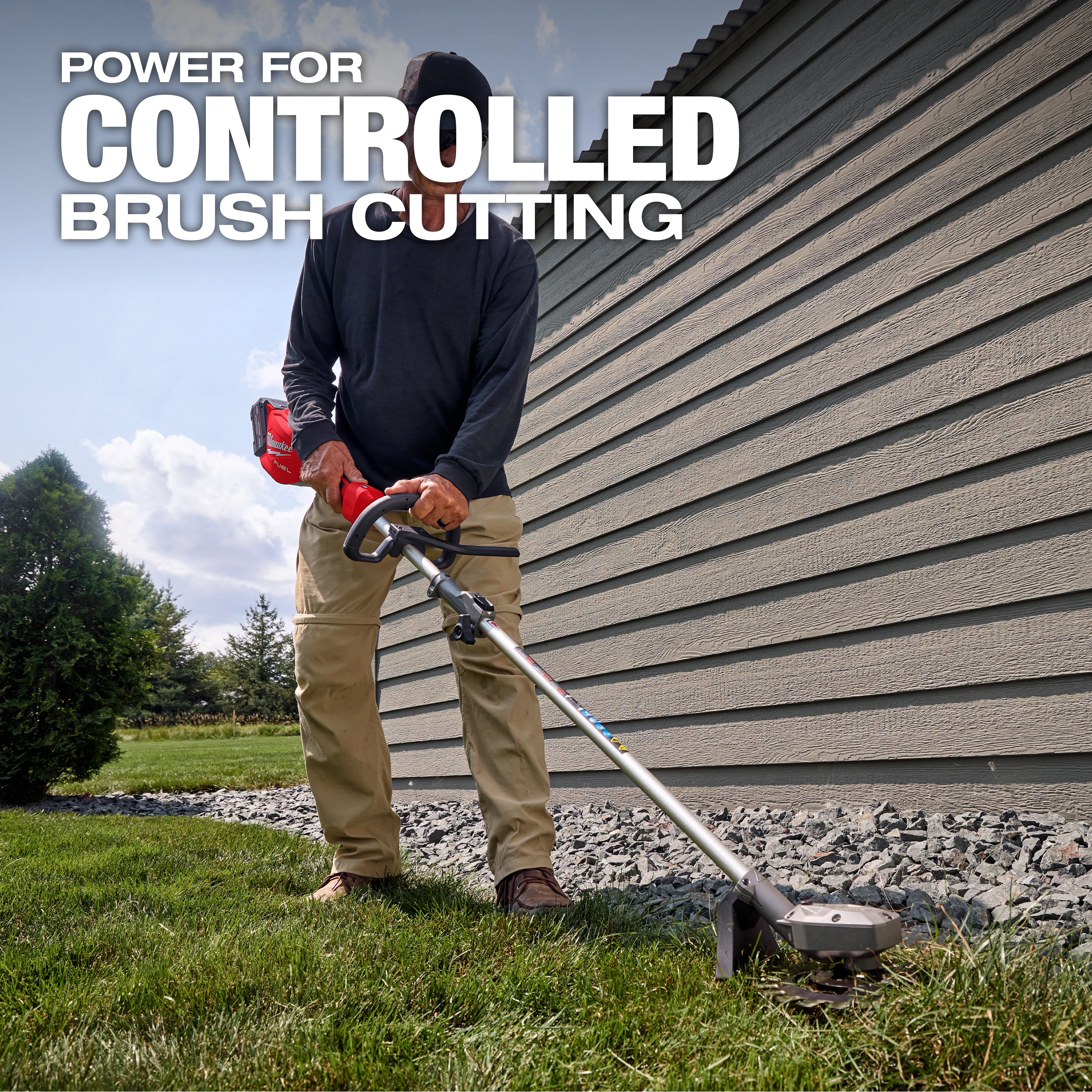 Person using an M18 FUEL QUIK-LOK Reciprocator Attachment to trim grass beside a building.