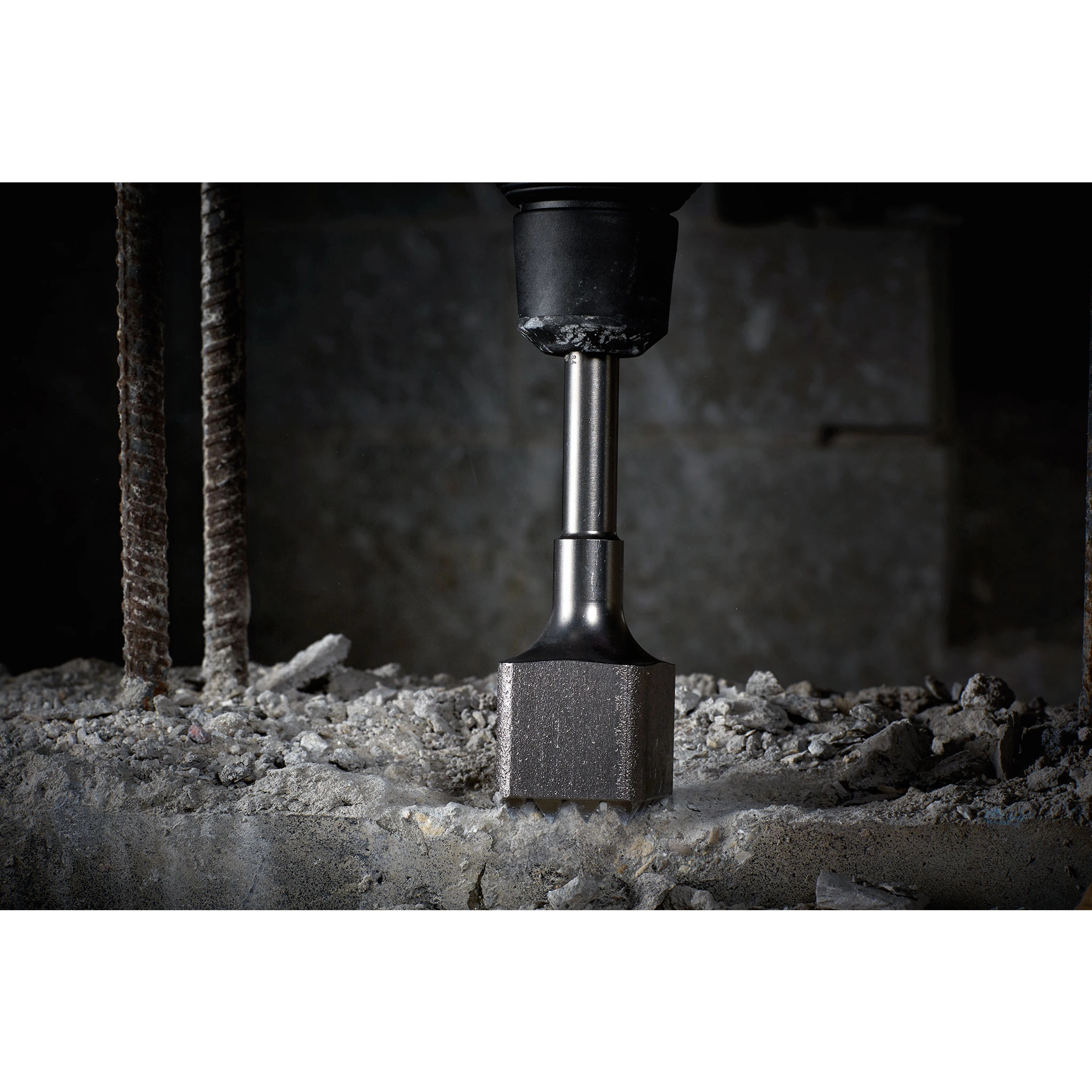 Bushing Tool at work on a concrete surface, chiseling away material. Rebar rods are visible on the left side of the image.