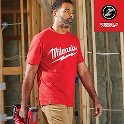 A man wearing a red Heavy Duty Tee Feature Shot with "Milwaukee" written in white, carrying a red power tool, in a construction setting.