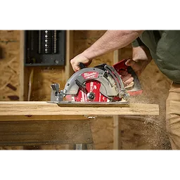A person is using a Milwaukee circular saw to cut through wood, causing sawdust to fly. The saw is equipped with a 7-1/4" 24T Worm Drive Framing Circular Saw Blade. The environment appears to be a woodworking or construction workspace.