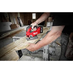 A person using the M18 FUEL Jigsaw, D-Handle to cut a piece of wood in a workshop environment.