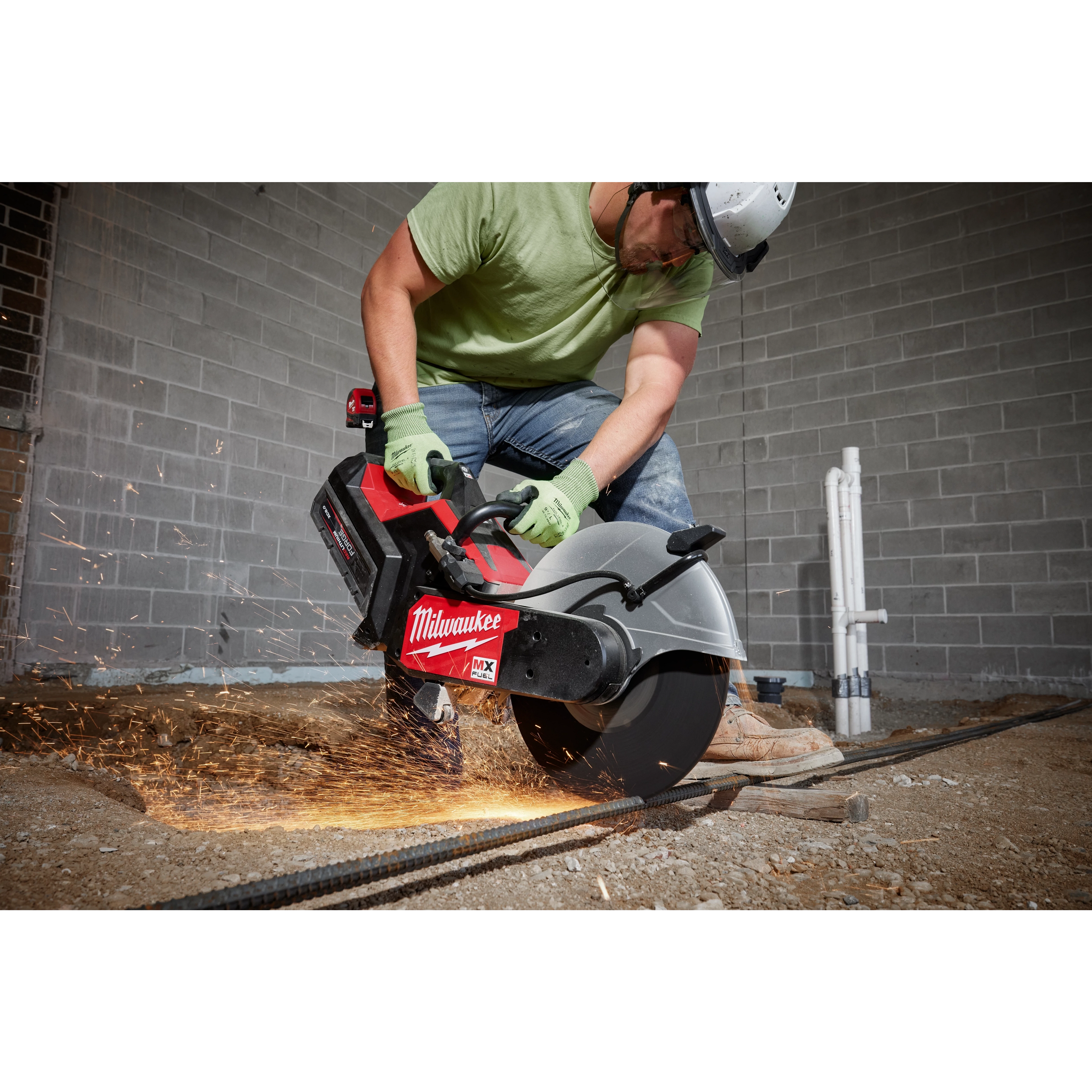 Worker in safety gear uses the MX FUEL 14" Cut-Off Saw with RAPIDSTOP, creating sparks while cutting metal rebar on the ground.