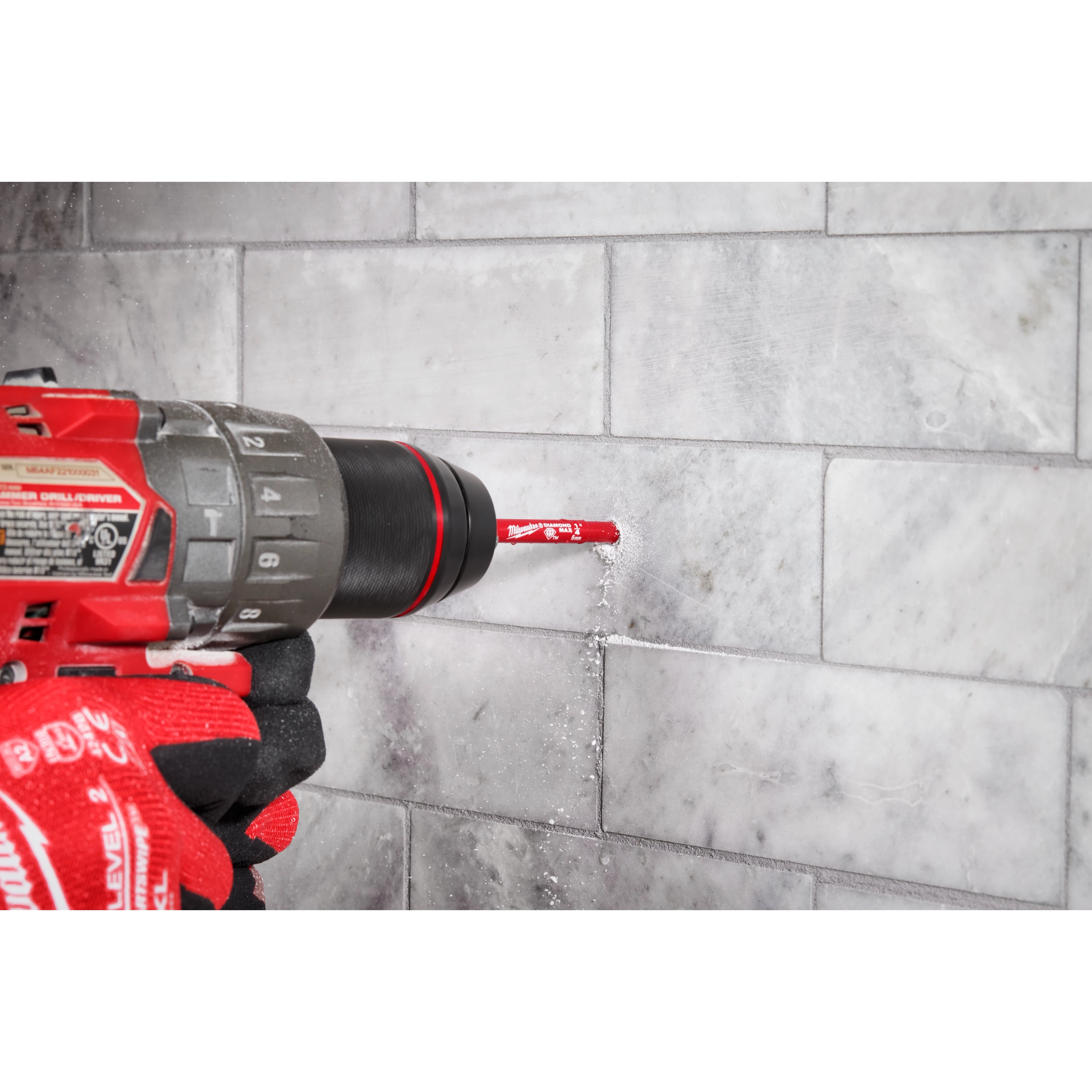 A Milwaukee® 1/4" DIAMOND MAX™ Hole Saw Bit is being used with a drill to cut into a tiled surface. A gloved hand is holding the drill steady as the drill bit creates a hole in the tiles. Dust and debris are visible around the drilling area.