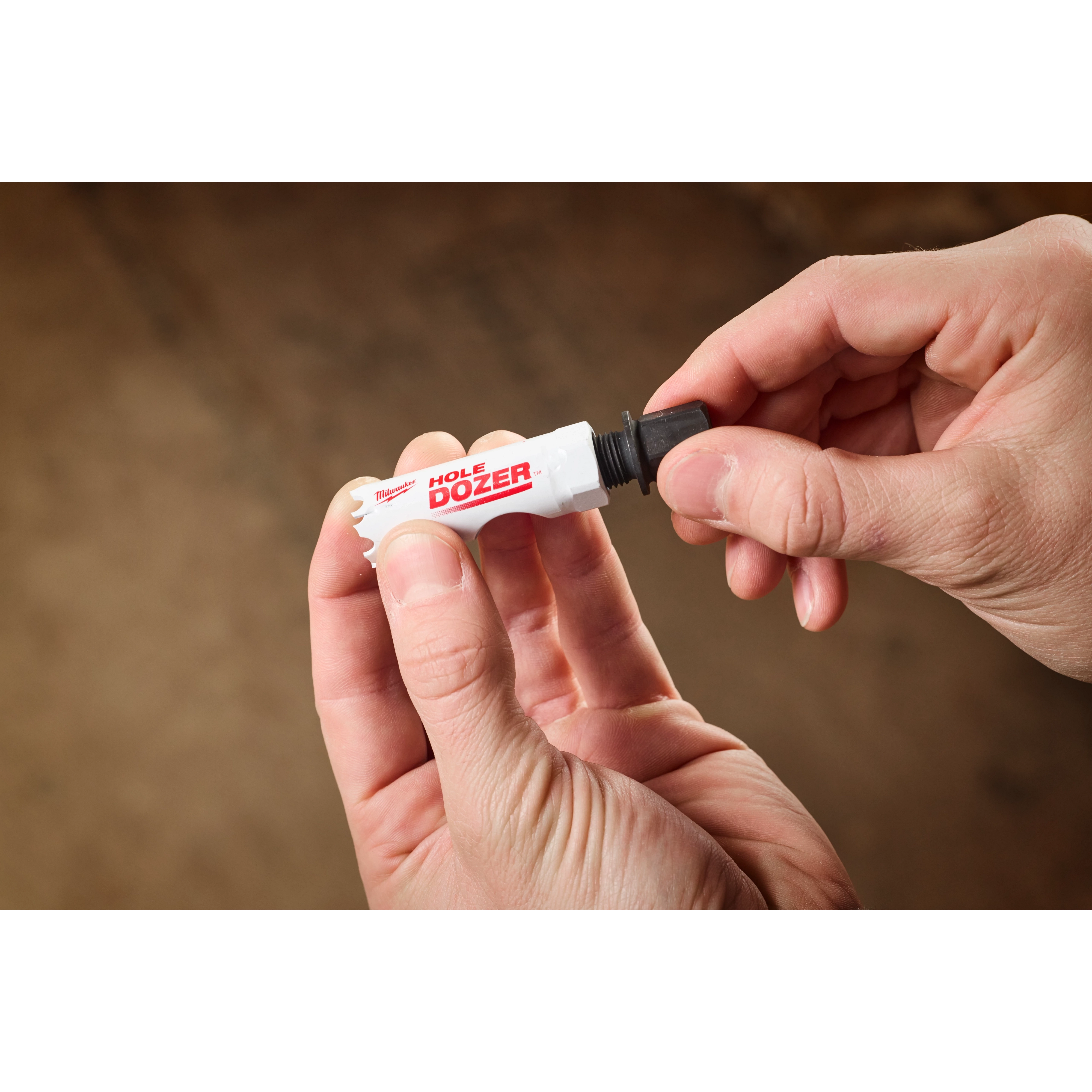 A person is holding a 5PK Small Adapter for QUIK-LOK™ Arbor in their hands. The adapter is labeled "HOLE DOZER" in red and white colors and has a threaded end for attachment.