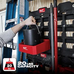 The PACKOUT Compact Shelf is red, mounted on a storage rack, and holds a black container. It has a 20 lbs capacity.