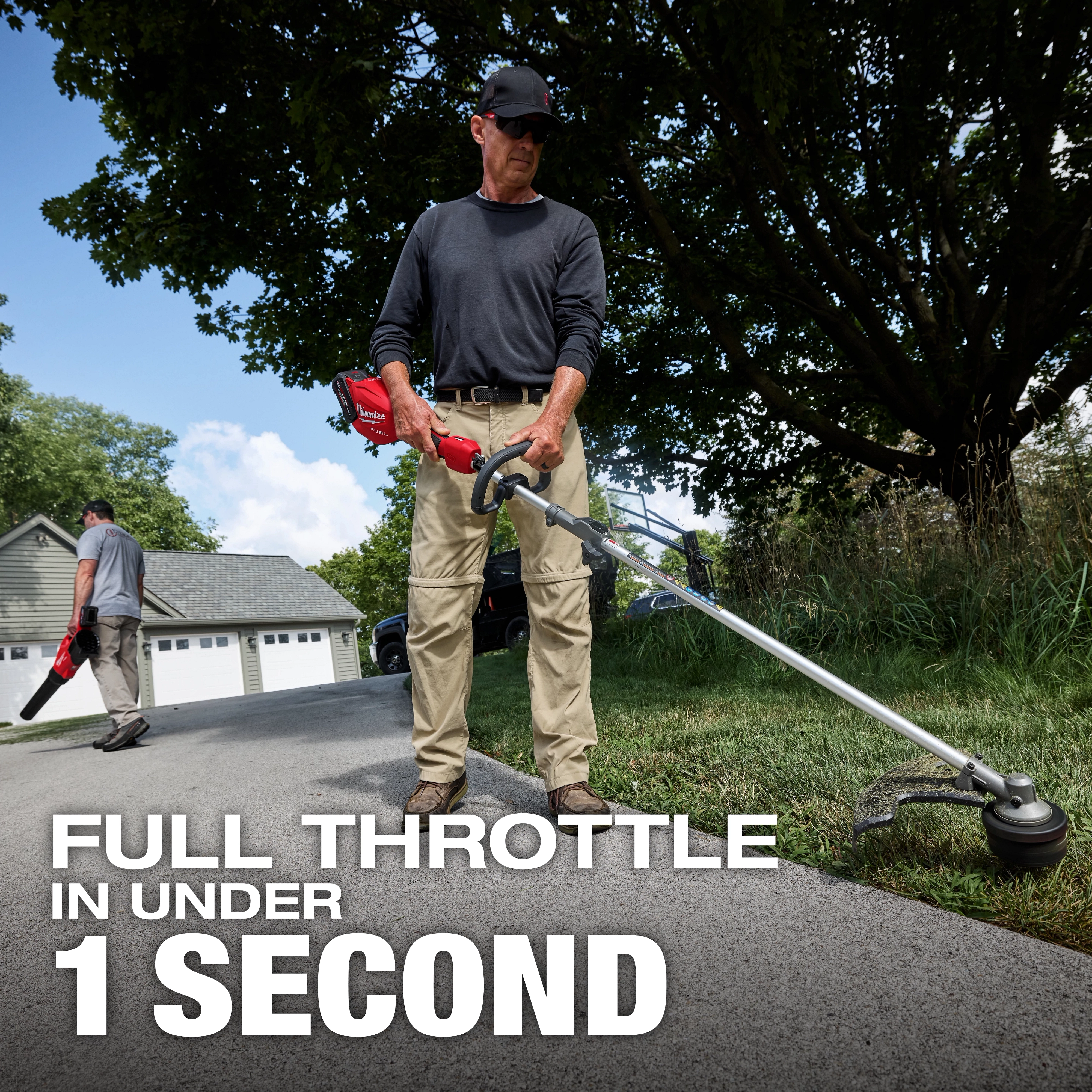 Worker using M18 FUEL String Trimmer w/ QUIK-LOK Kit along a paved driveway.