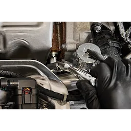 A gloved hand uses a 1/4" Drive 6mm Low-Profile Hex Bit Socket to tighten or loosen a bolt in a compact space within an engine compartment. The socket is attached to a ratchet, facilitating precise adjustments.