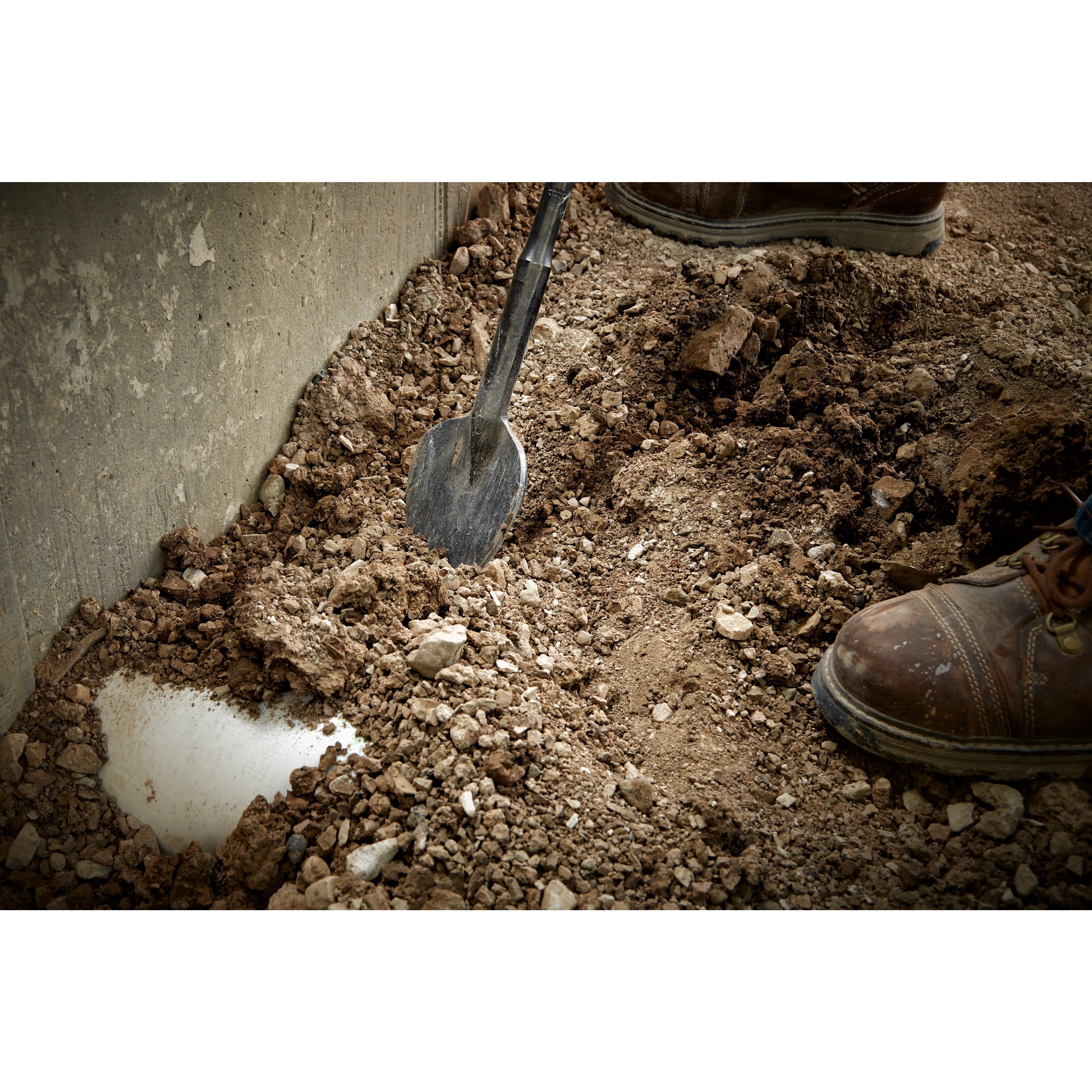 SDSMAX 4.25" X 16" CLAY SPADE digging into compact soil near a concrete structure, with a worker wearing brown boots nearby.