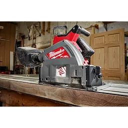 Milwaukee M18 FUEL 6 1/2" Plunge Track Saw placed on a wooden surface in a workshop with tools and doors in the background.