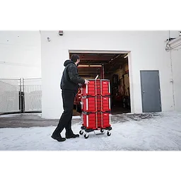 A person pushes a 366pc. Master Mechanics Hand Tool Set with PACKOUT™ Drawers and Dolly into a garage. The tool set is stacked in red, wheeled drawers, and the scene is outdoors with snow on the ground.