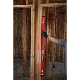 Person using a REDSTICK Level on wooden frame construction. The level has a red body, three spirit vials, and is held vertically.