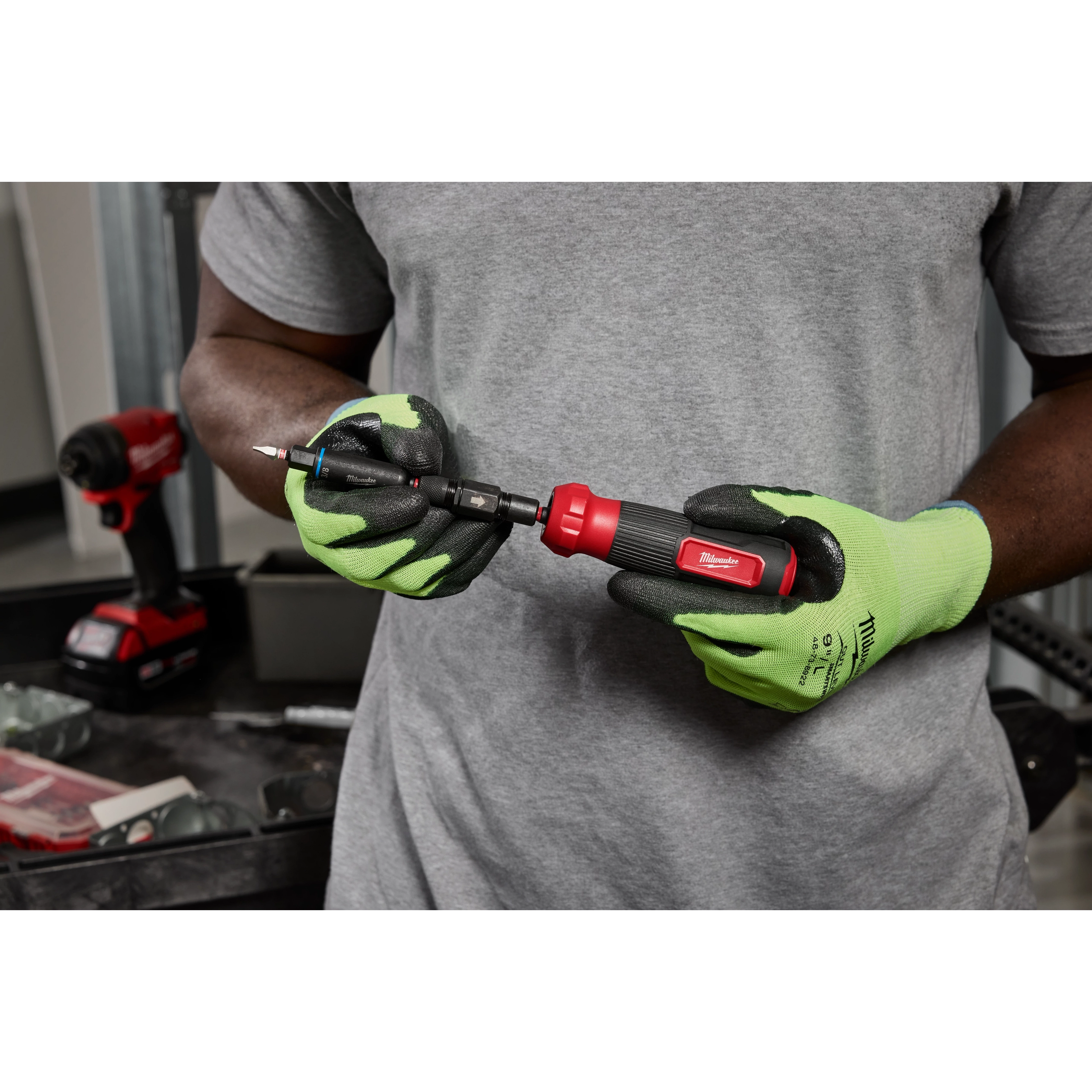 A person holds the Milwaukee 8-IN-1 Multi-Bit & Nut Driver W/ SHOCKWAVE Impact Duty Bits & Nut Drivers in their hands. The tool has a red handle and interchangeable bits, designed for impact duty applications.