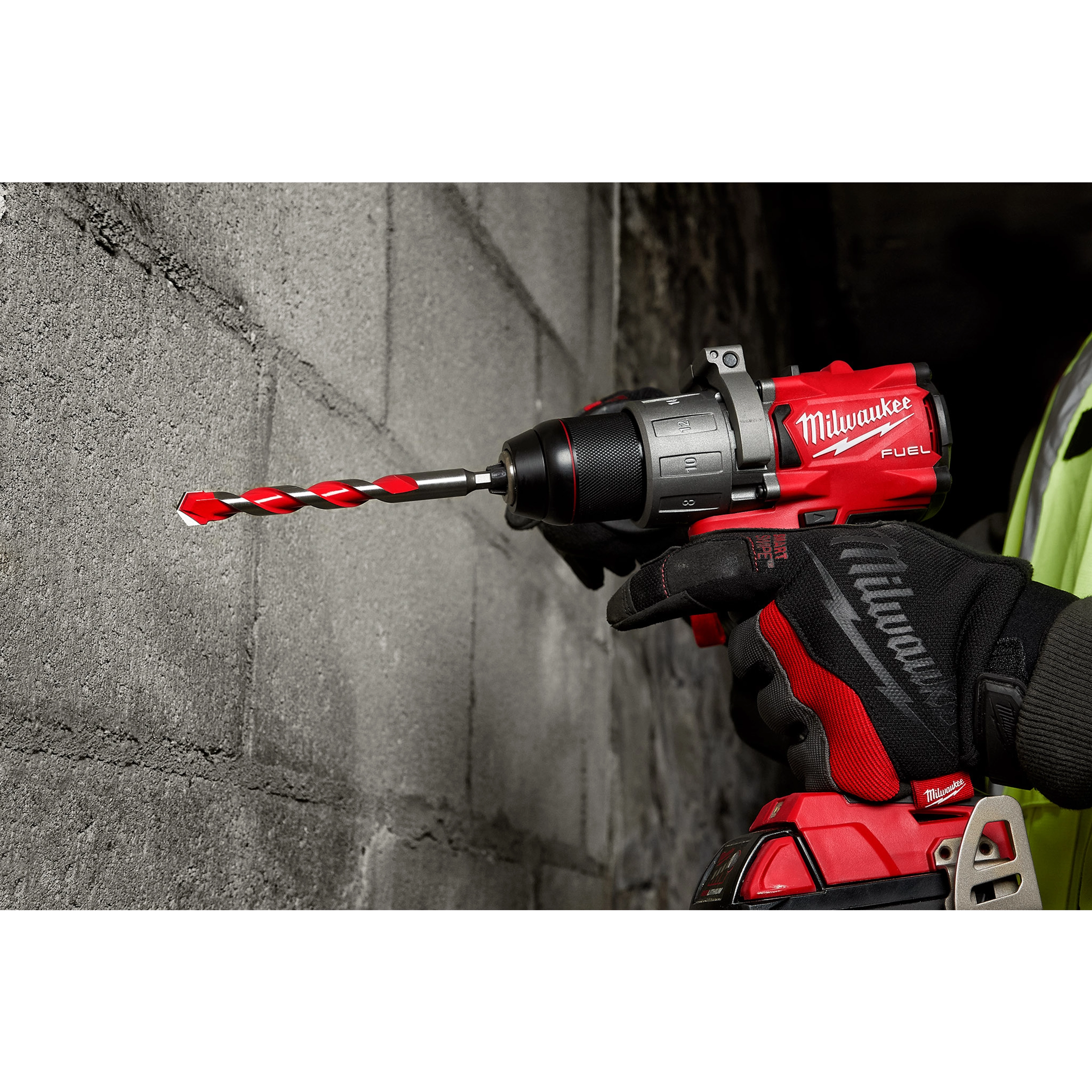 Close-up of a person using a red and black drill with a Shockwave Carbide Hammer Drill Bit, 1/2", drilling into a concrete wall.